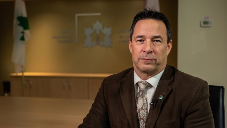 A man sits in an office at the Canadian Home Builders' Association wearing a white shirt and brown suit. 