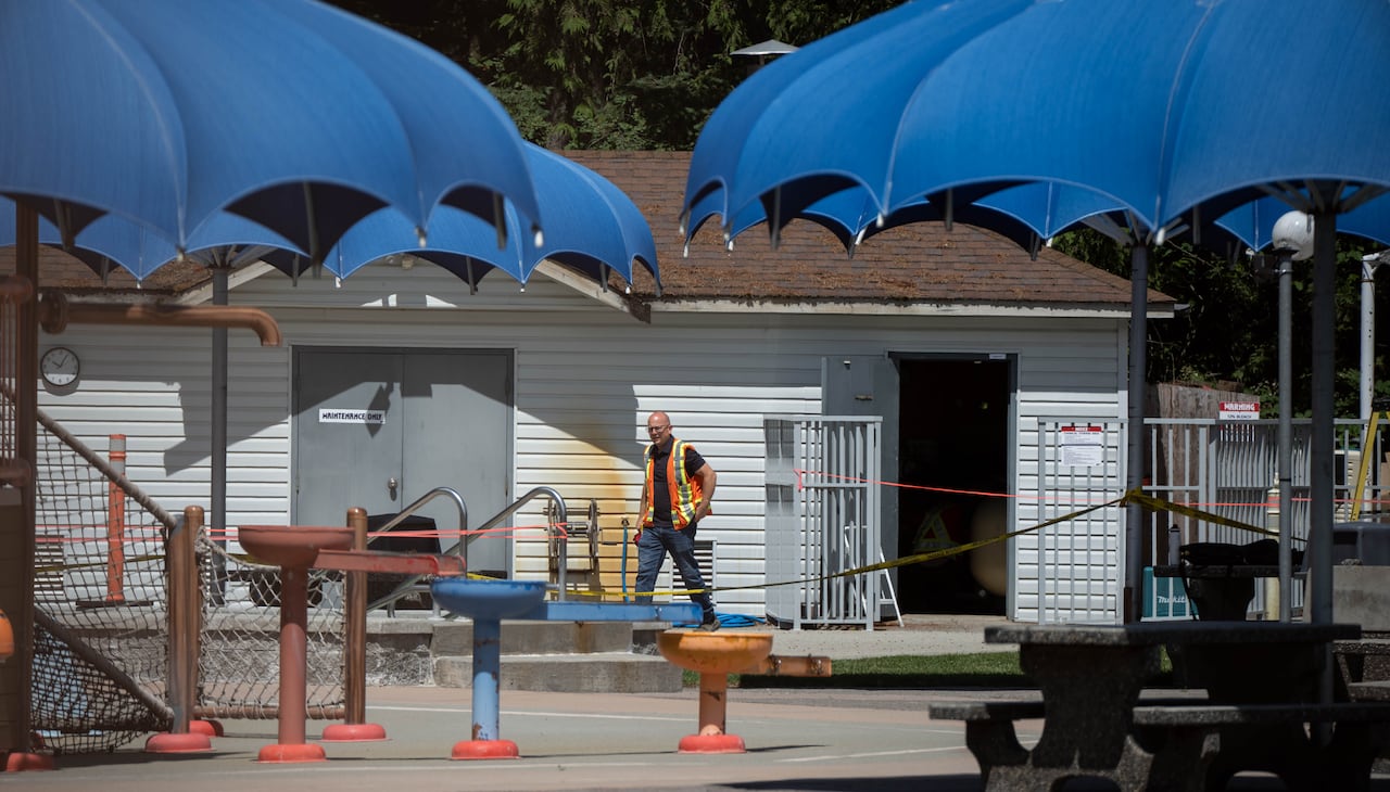 A man in an orange and yellow work vest walks behind caution tape with patio umbrellas in the foreground.